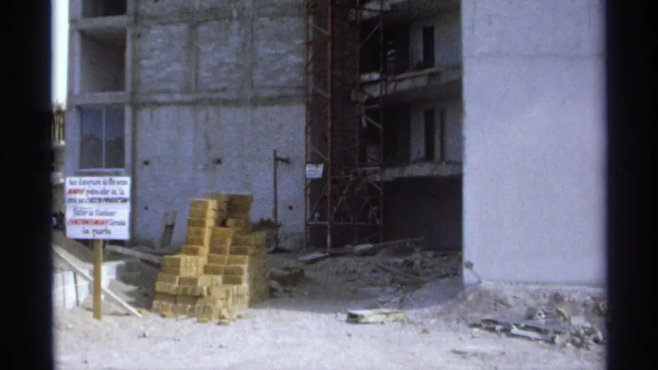 1975 Guaymas construction site with an unfinished concrete facade, stacked bricks, scaffolding, debris, and a Spanish sign in view.