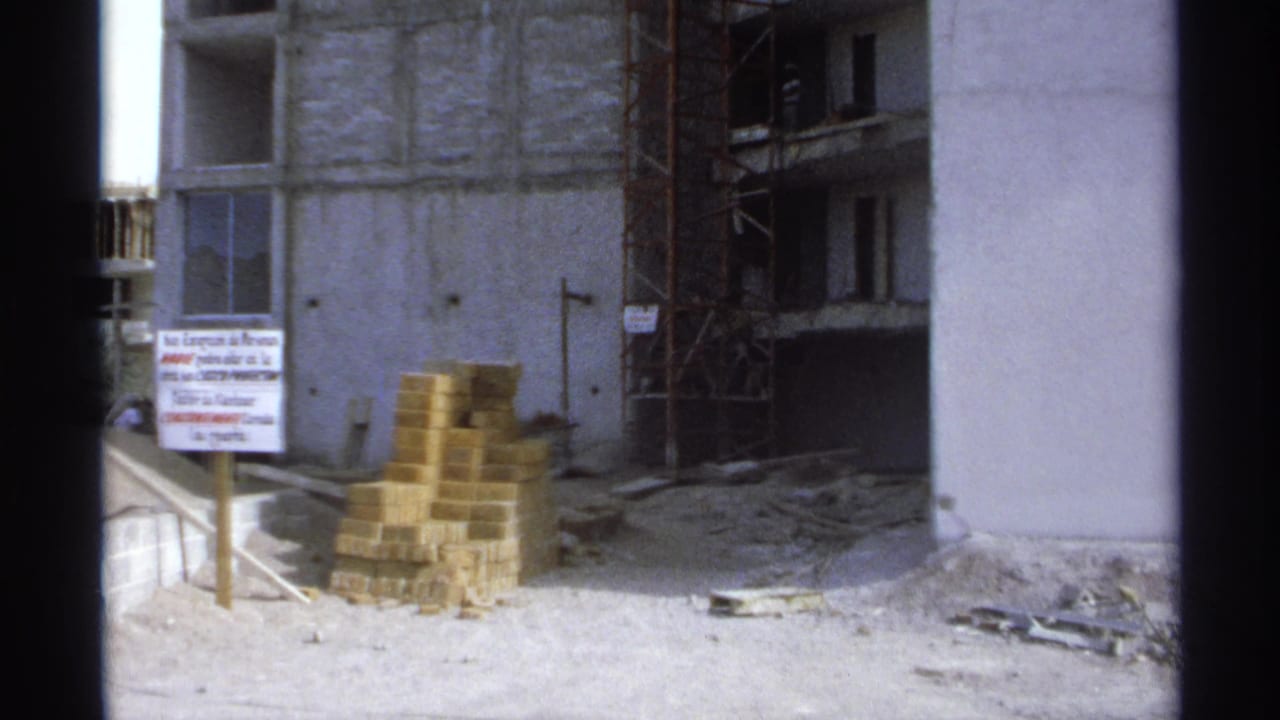 Construction site with brick stacks, scaffolding, concrete columns, and a sign in Spanish.
