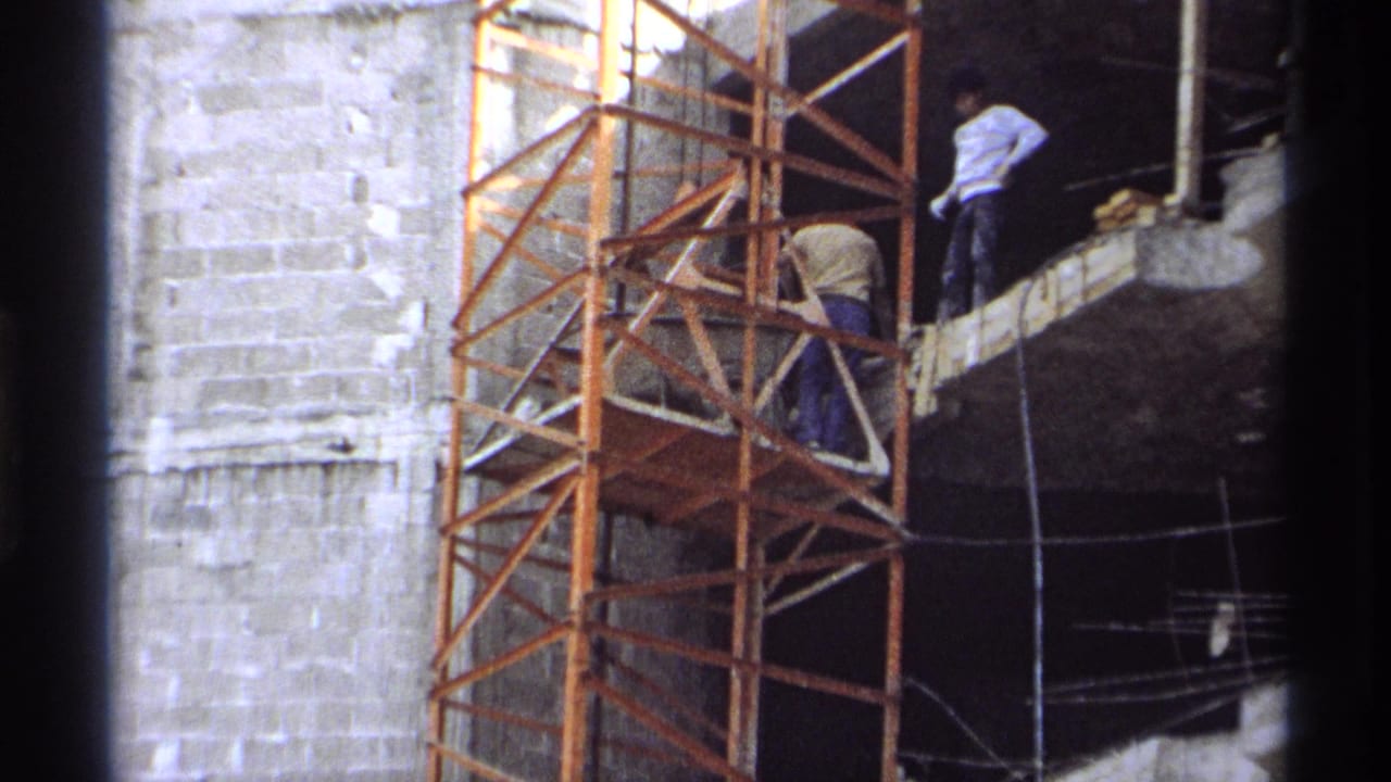 1975 Guaymas 8mm frame showing workers on an orange scaffold at a concrete building site.