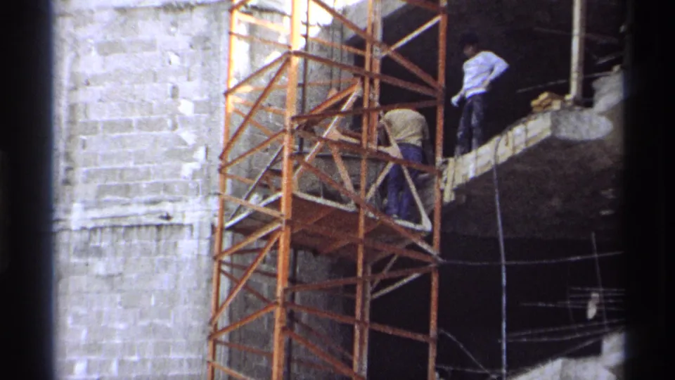 1975 Guaymas 8mm frame showing workers on an orange scaffold at a concrete building site.