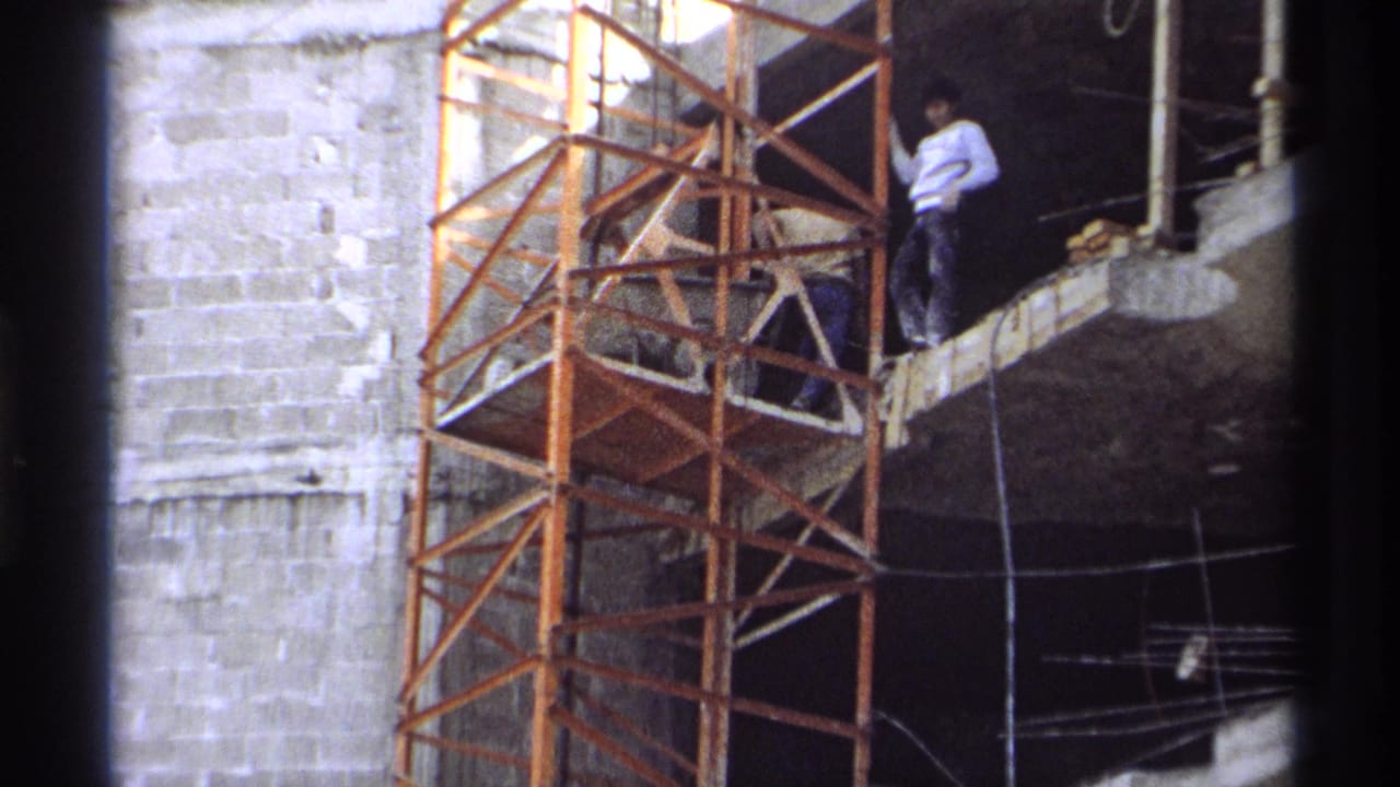 Workers stand near scaffold platforms on a partially built concrete structure.