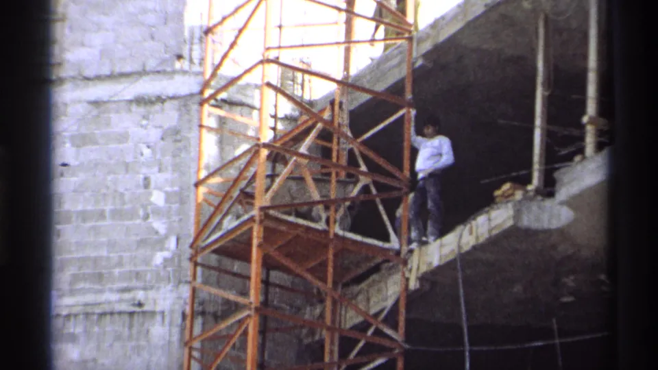 1975 Guaymas construction frame showing a worker by orange scaffolding and an unfinished concrete wall.