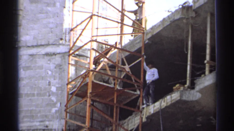 1975 Guaymas 8mm frame of a worker near an orange scaffold on an unfinished concrete building.