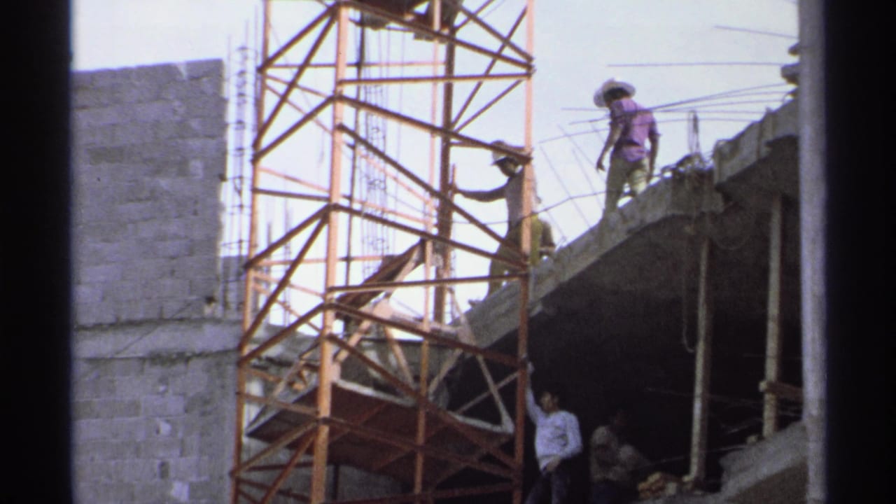 Construction workers stand near scaffolding on the edge of an unfinished building.