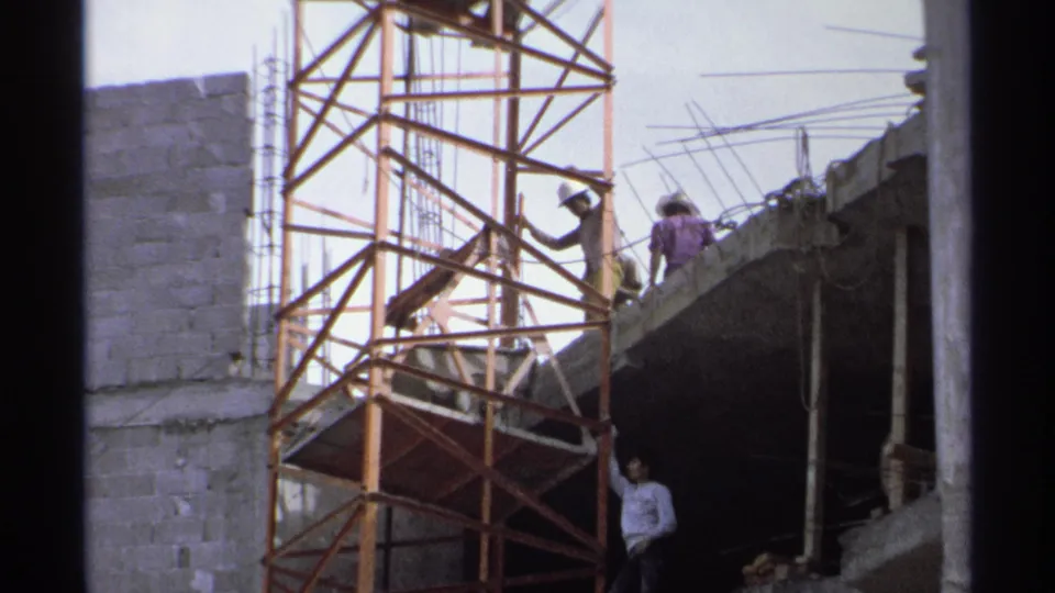 1975 Guaymas, Mexico construction site with scaffold sections, workers, rough concrete walls, and exposed reinforcing bars.