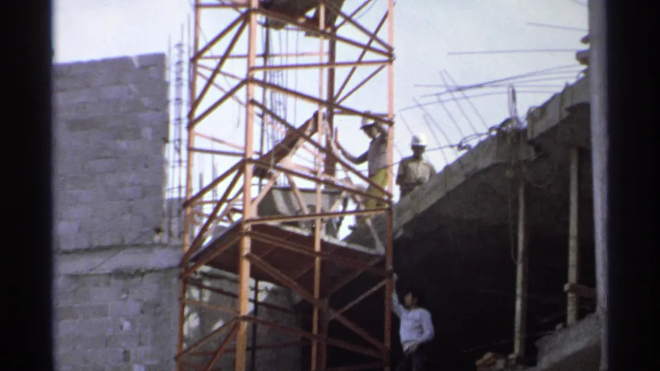 1975 Guaymas, Mexico 8mm frame showing workers on a building site with scaffolding, concrete block walls, and rebar.