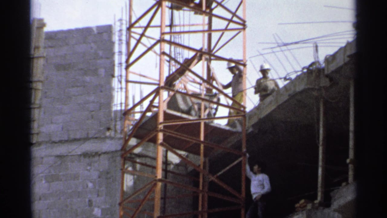 1975 Guaymas construction site with workers on scaffolding near exposed rebar, cinder block walls, and an unfinished concrete floor.