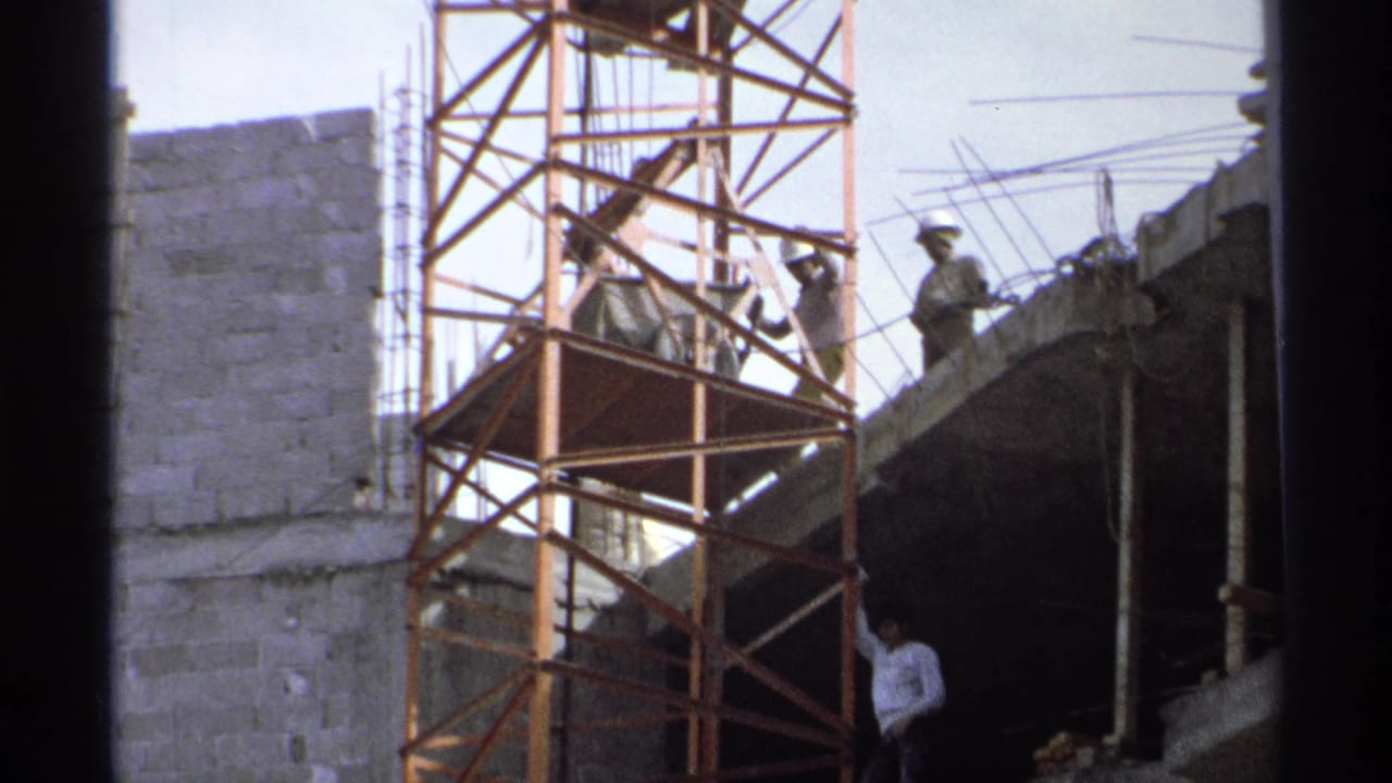 Scaffold tower and workers beside a partially built concrete structure.