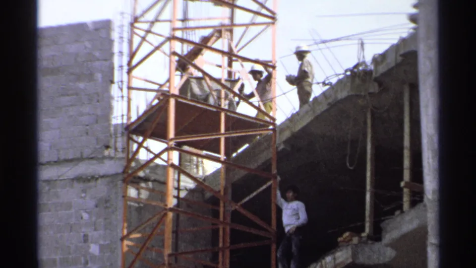 At the Guaymas construction site, workers stand on scaffold platforms and the slab edge while another man is visible below in shadow.