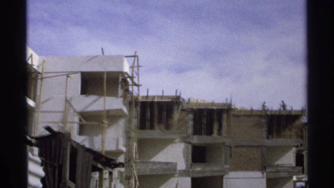 Unfinished multi-story building with scaffolding and workers under a blue sky.