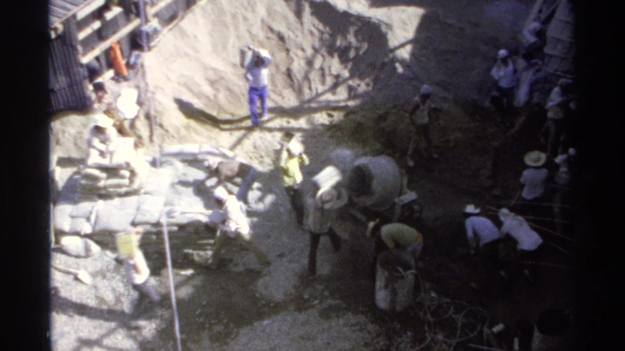 Workers at a construction site near a sand pile and cement mixer.