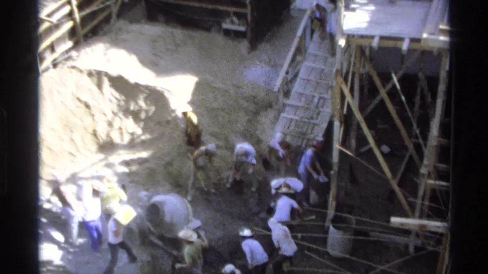 Final 1975 Guaymas frame showing workers spread across a construction site with scaffolding, sacks, and a cement mixer below.