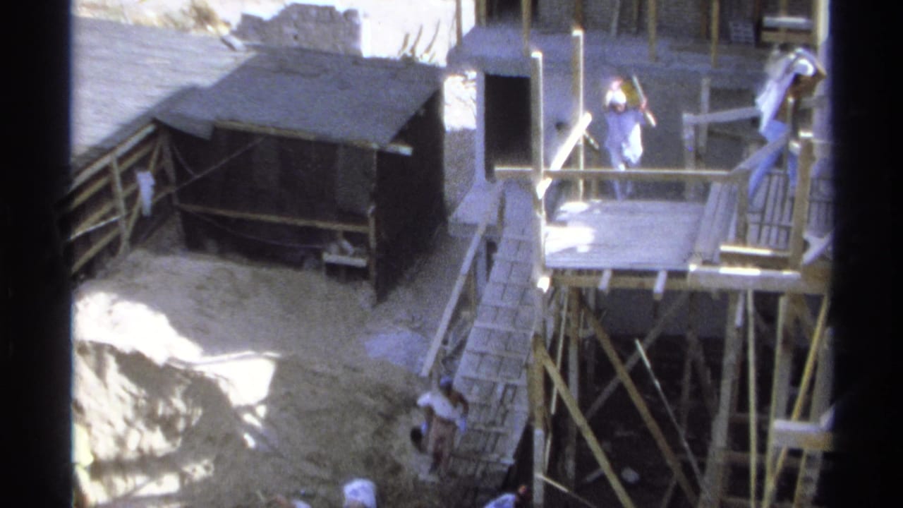 Raised wooden platform, scaffolding, shed, and workers around a construction area.