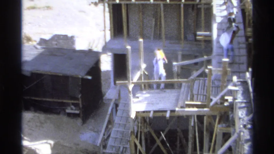 Home-movie frame from Guaymas in 1975 showing a worker on a raised platform among wooden scaffolding and formwork.