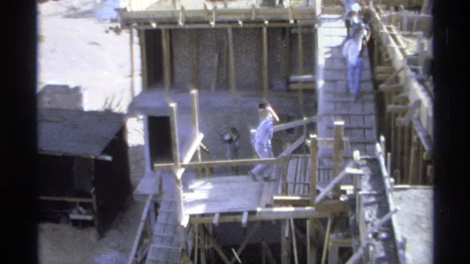 1975 Guaymas 8mm frame with a worker crossing near wood railings, scaffolding, a ladder, and a small shed at a building site.