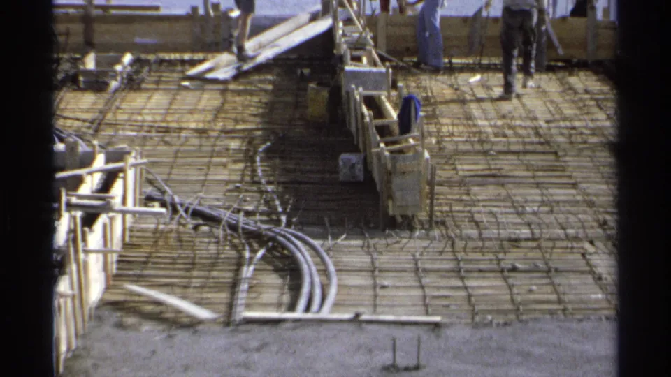 1975 Guaymas construction site view showing rebar, conduits, wood forms, equipment, and workers partly cropped near the top of frame.