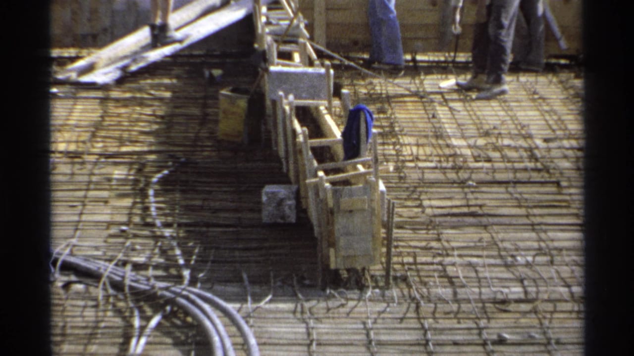 Foundation deck with rebar, wood forms, conduits, and workers standing near the upper edge.