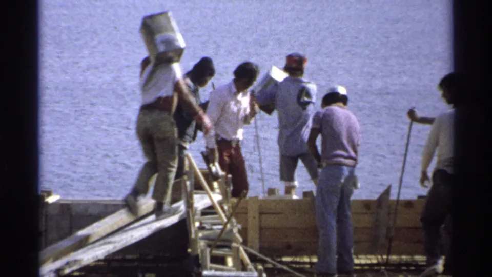 Guaymas waterfront construction scene with men, ladders, wood forms, and hand-carried materials on 8mm film.