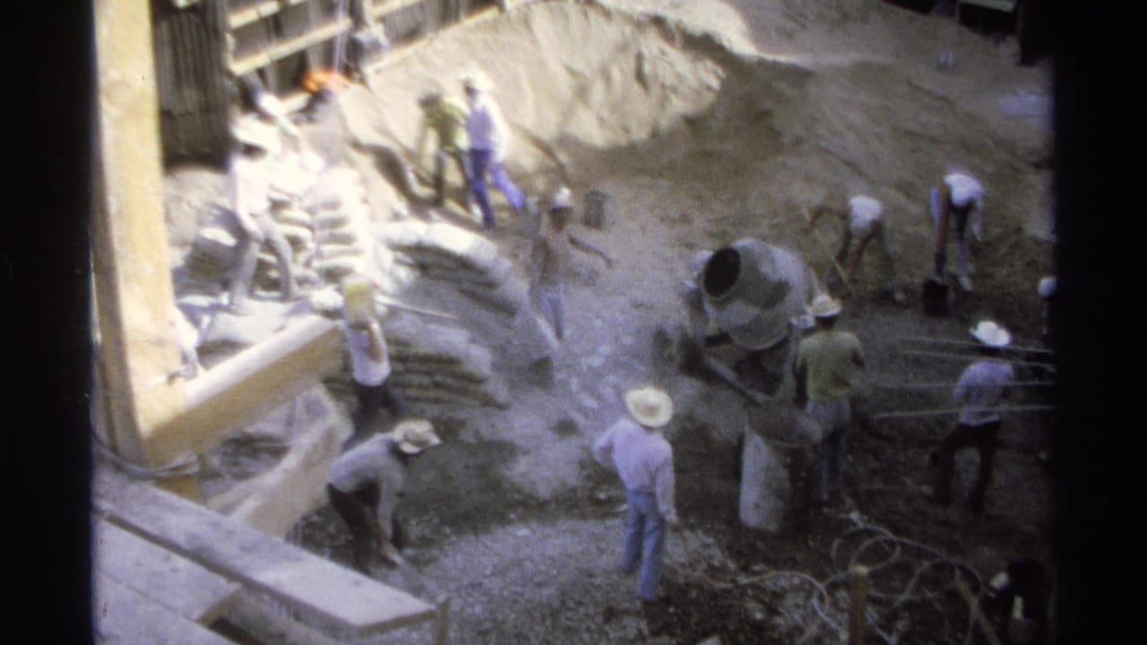 1975 Guaymas construction scene with men in white hats working around excavation, formwork, bags, and a cement mixer.