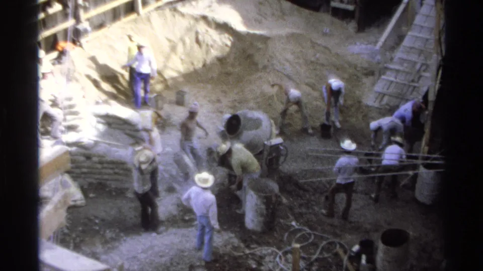Elevated 8mm view of men working at a 1975 Guaymas building site with a mixer, hoses, bags, and timber formwork.