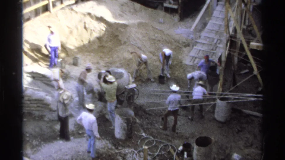 The construction site remains active as men shovel and move around the mixer, ladder, timber forms, and excavation in Guaymas.