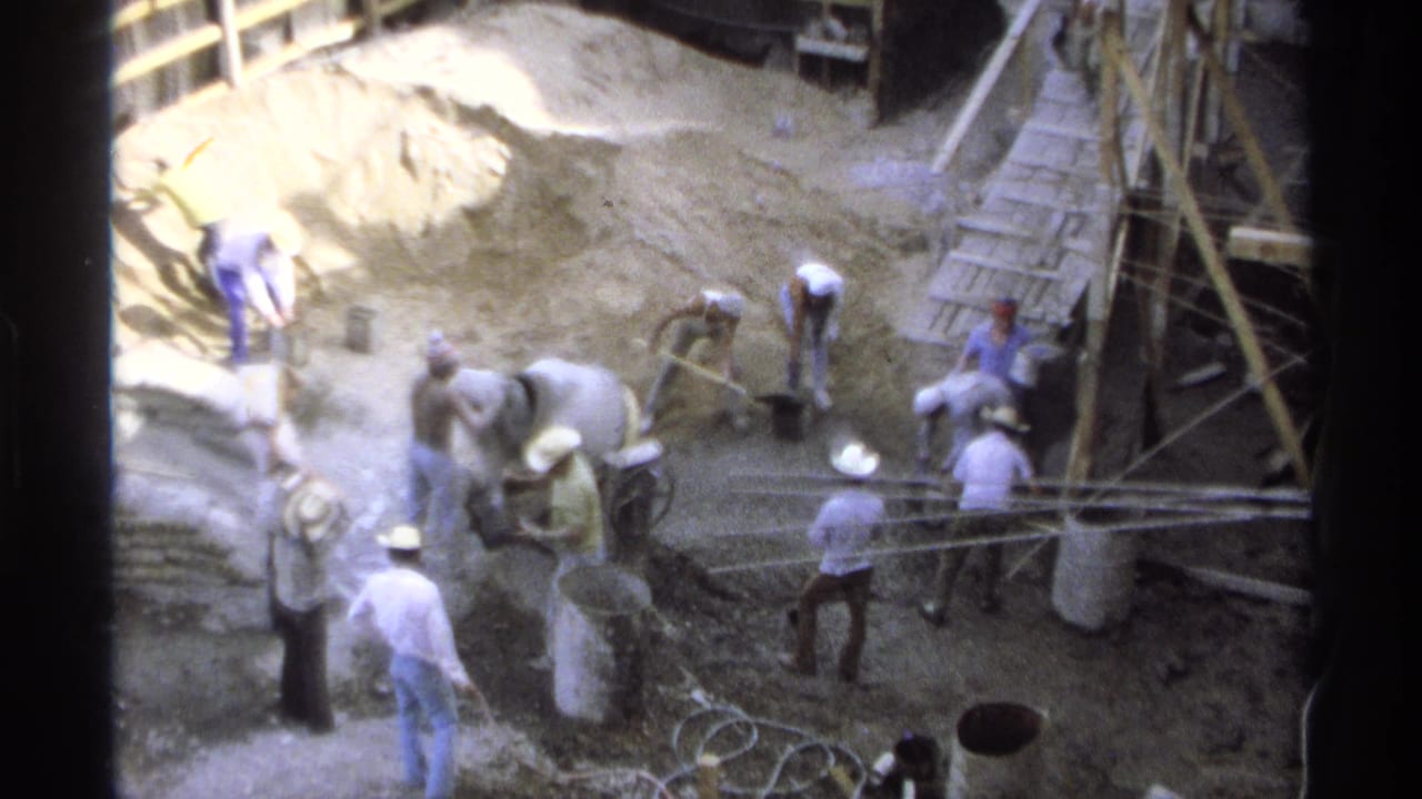 High-angle view of workers around a cement mixer and sand pile at a construction site.