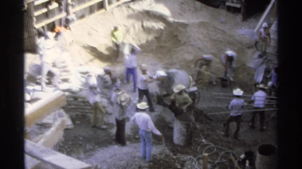 High-angle 8mm frame from Guaymas in 1975 showing workers clustered around sand, buckets, and construction equipment.