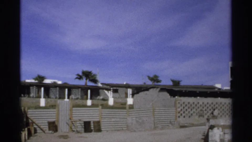 Guaymas residential exterior with palm trees, corrugated site walls, and a low flat-roof house in 1975 home-movie footage.