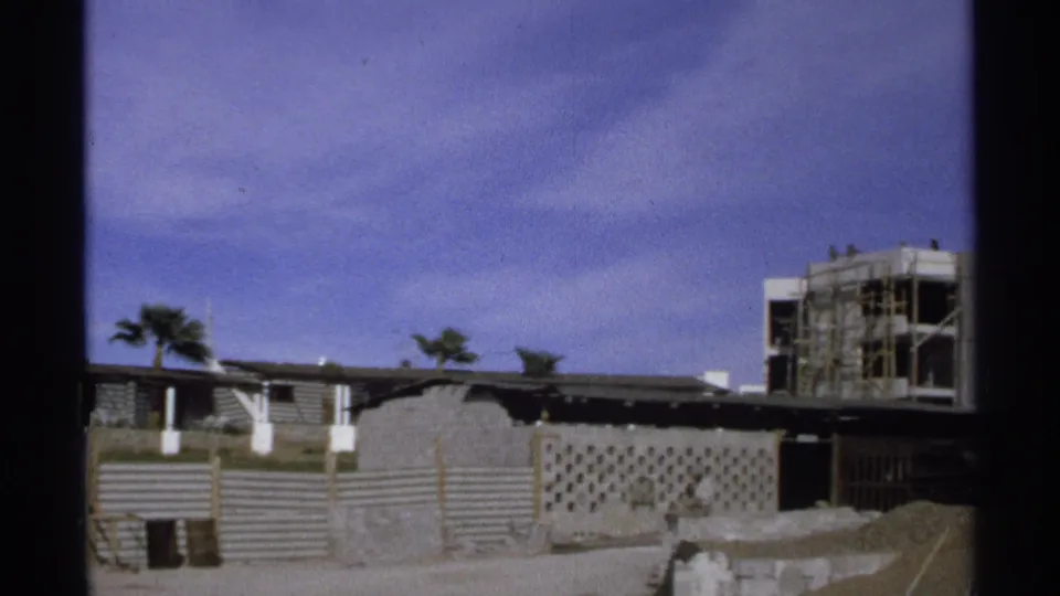 A Guaymas construction view shows palm trees, corrugated barriers, and a partially built structure with scaffolding in 1975.