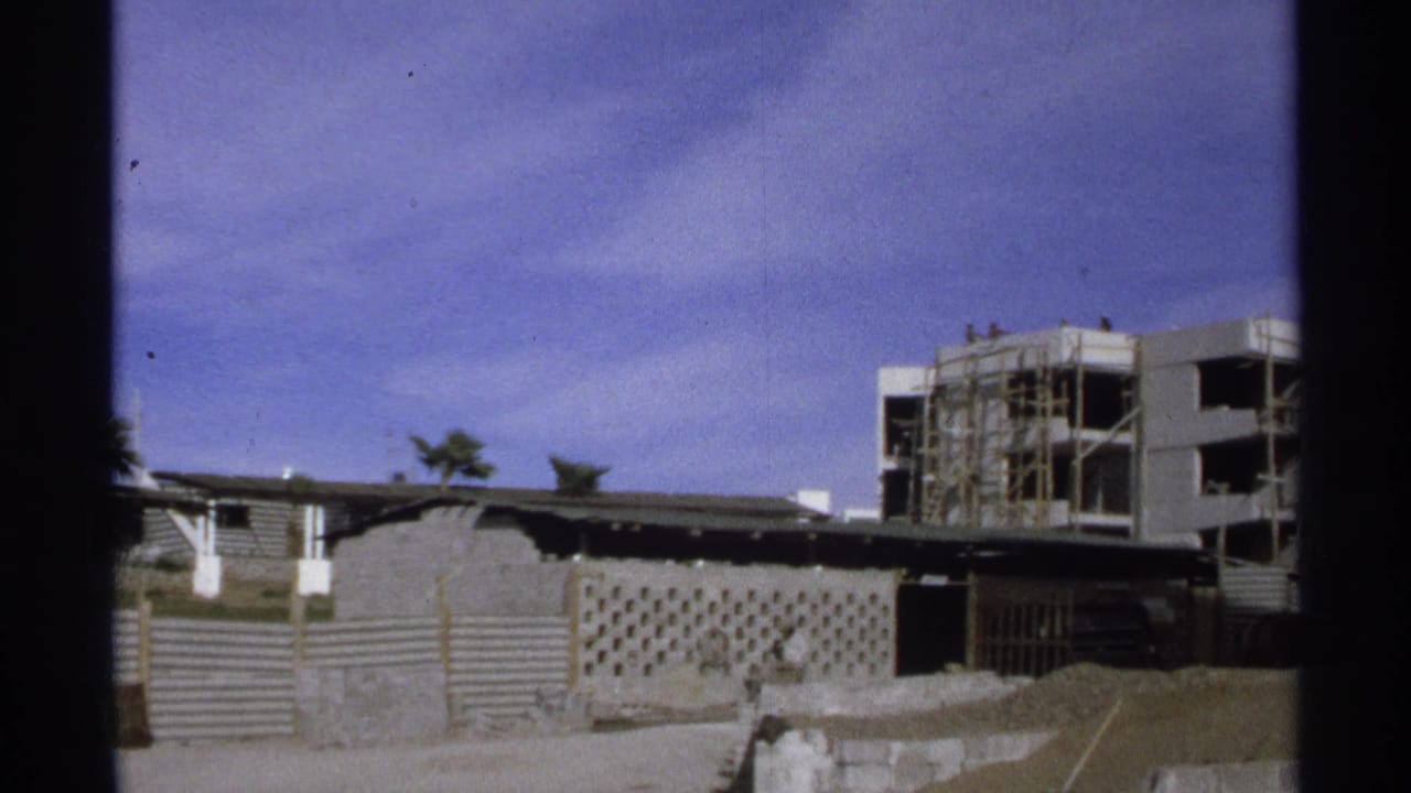 1975 Guaymas home-movie frame showing a construction site, scaffolding, fencing, and an unfinished multi-story building.