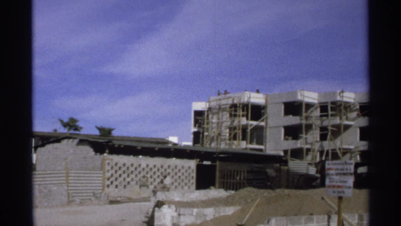 Unfinished building and scaffolded construction area behind fencing and a sign.
