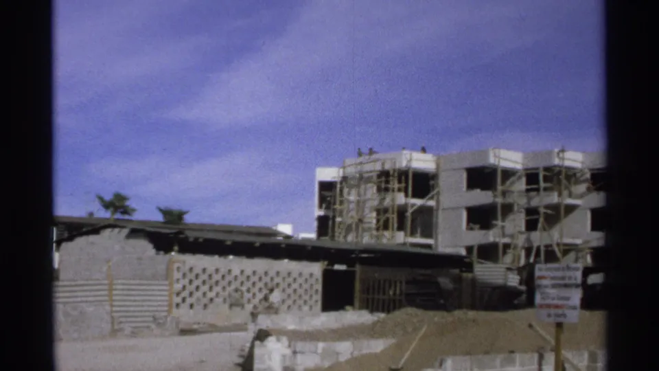 Guaymas, Mexico construction view with scaffolding, an unfinished concrete building, fencing, and a posted sign near the street.