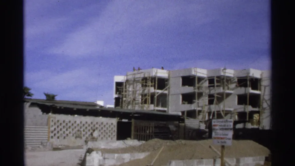 1975 Guaymas frame with a closer view of a scaffolded construction site, low walls, fencing, and a sign at the right edge.