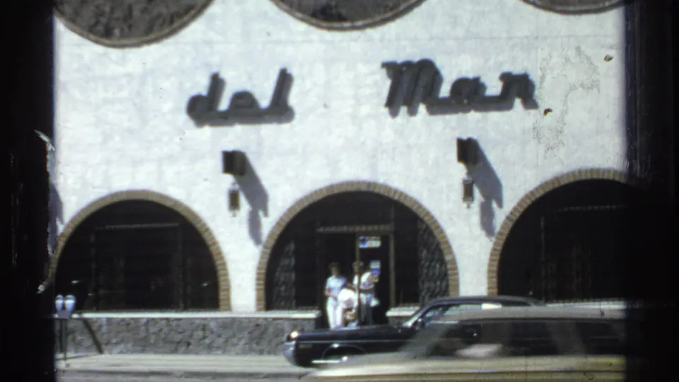 Guaymas, Mexico street view of a white arched building marked del Mar, with people by the entrance and a black car passing or parked nearby.