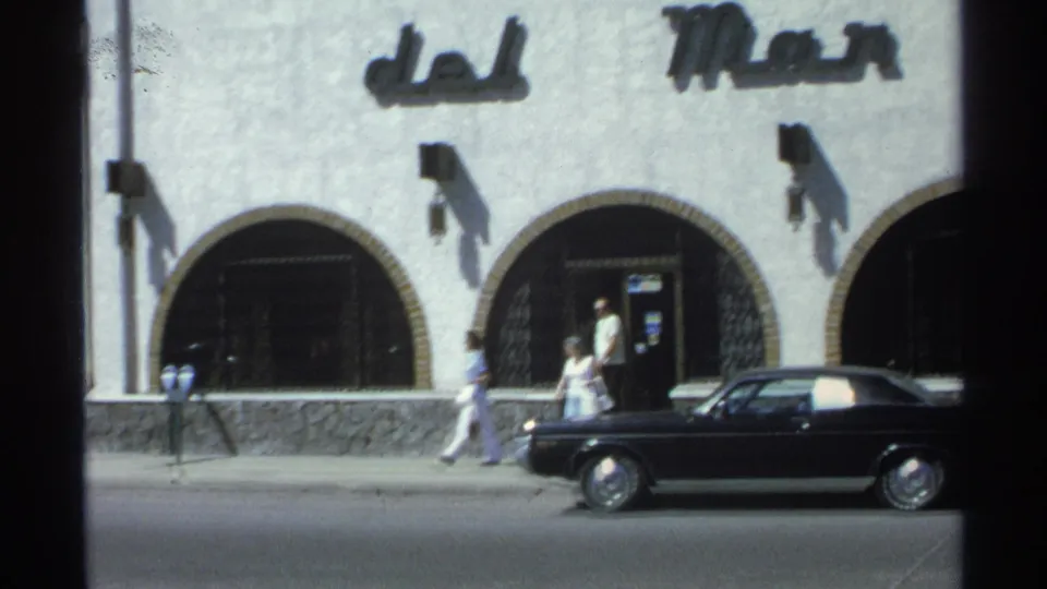 Guaymas, Mexico street frame from 1975 showing pedestrians passing arched openings beneath del Mar signage and a parked black car.