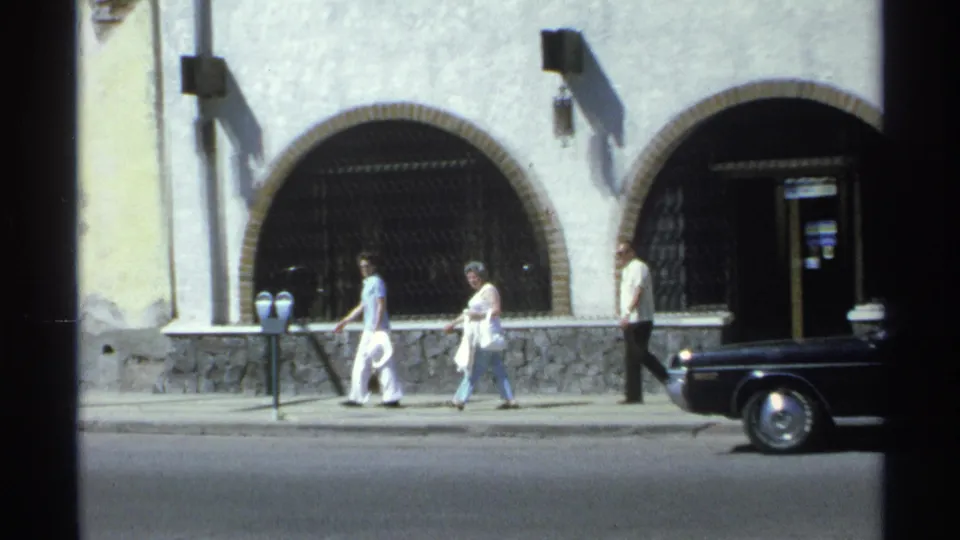 Guaymas, Mexico 1975 street frame with pedestrians, parking meters, arched doorways, and a black coupe partly leaving the shot.