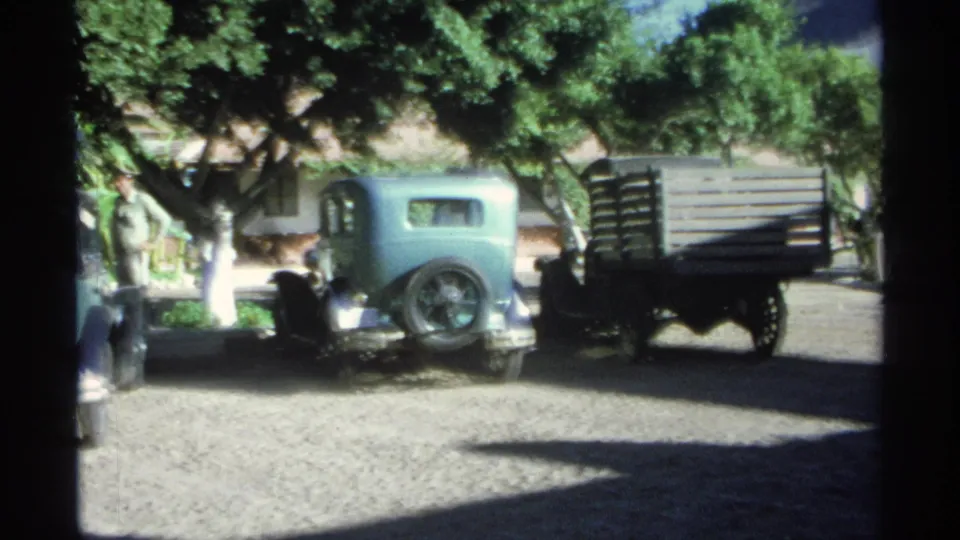 1975 Guaymas frame showing a teal older car beside a wooden-sided truck in a bright street scene.