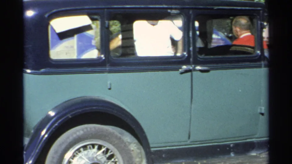 A green sedan with a dark roof is shown in side view, with people visible inside the car in Guaymas, 1975.