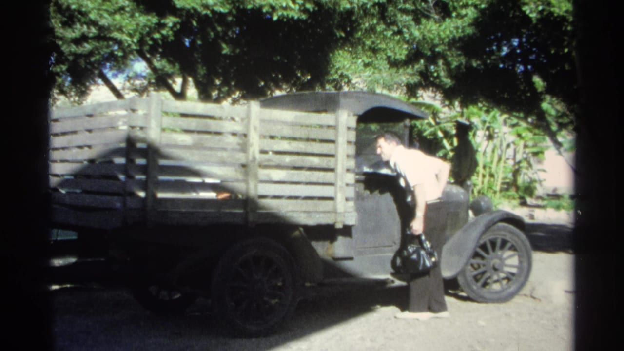 Man in a white shirt leans beside a black pickup truck with a wooden slat bed.