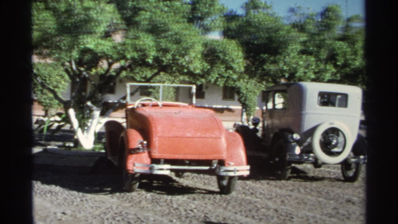 Red convertible and white vintage sedan parked side by side in a sunny gravel lot.