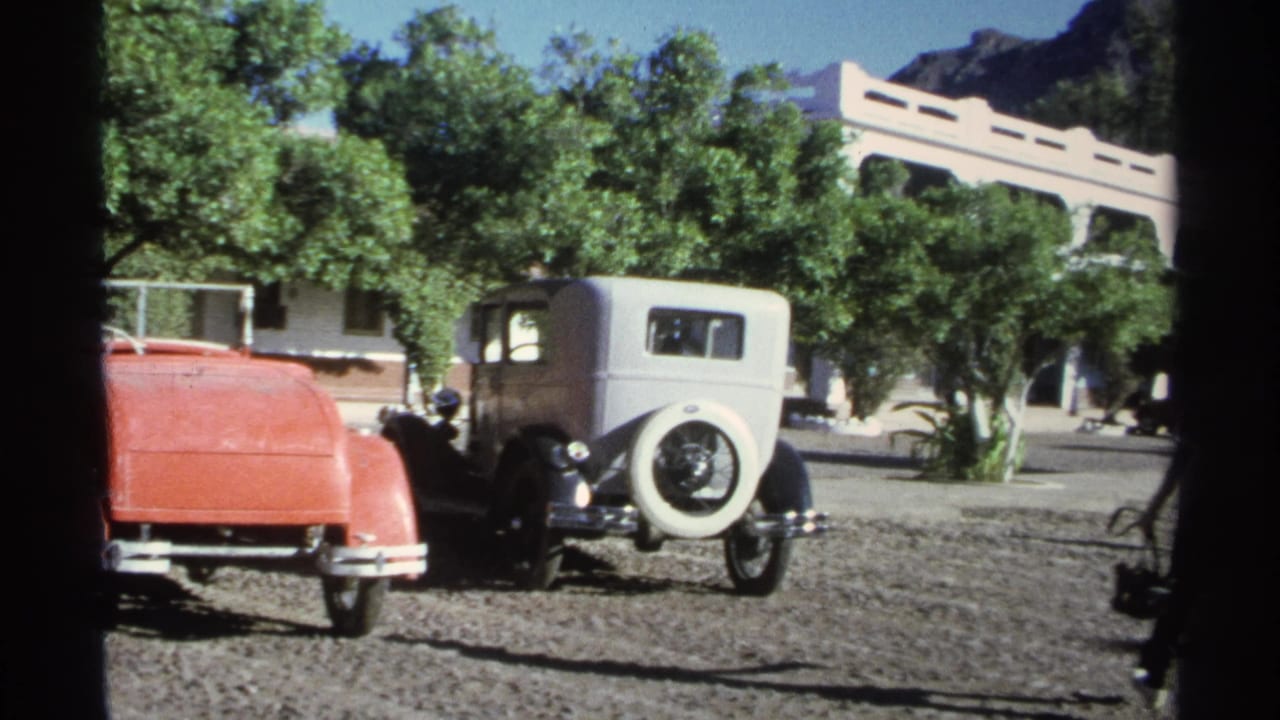 1975 Guaymas home-movie frame showing vintage cars in a resort parking area below trees and a pale building.