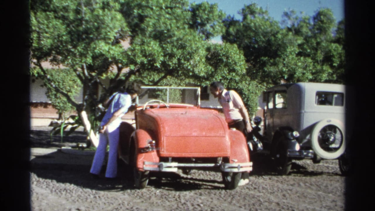 A 1975 Guaymas home-movie frame shows adults clustered around a red convertible with trees and a gray sedan behind it.