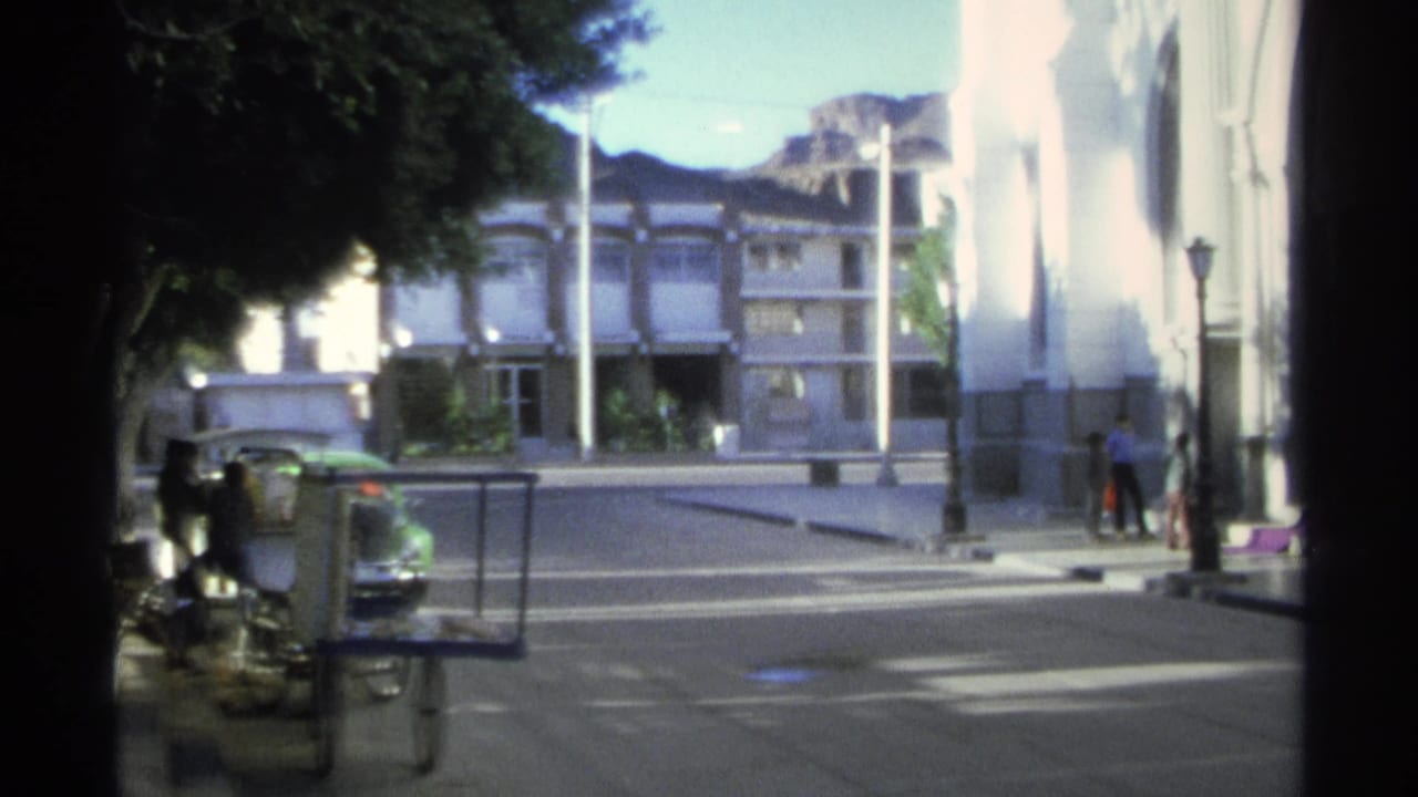 The clip ends on a Guaymas street view with buildings, trees, parked vehicles, and small adult figures near the sidewalk.