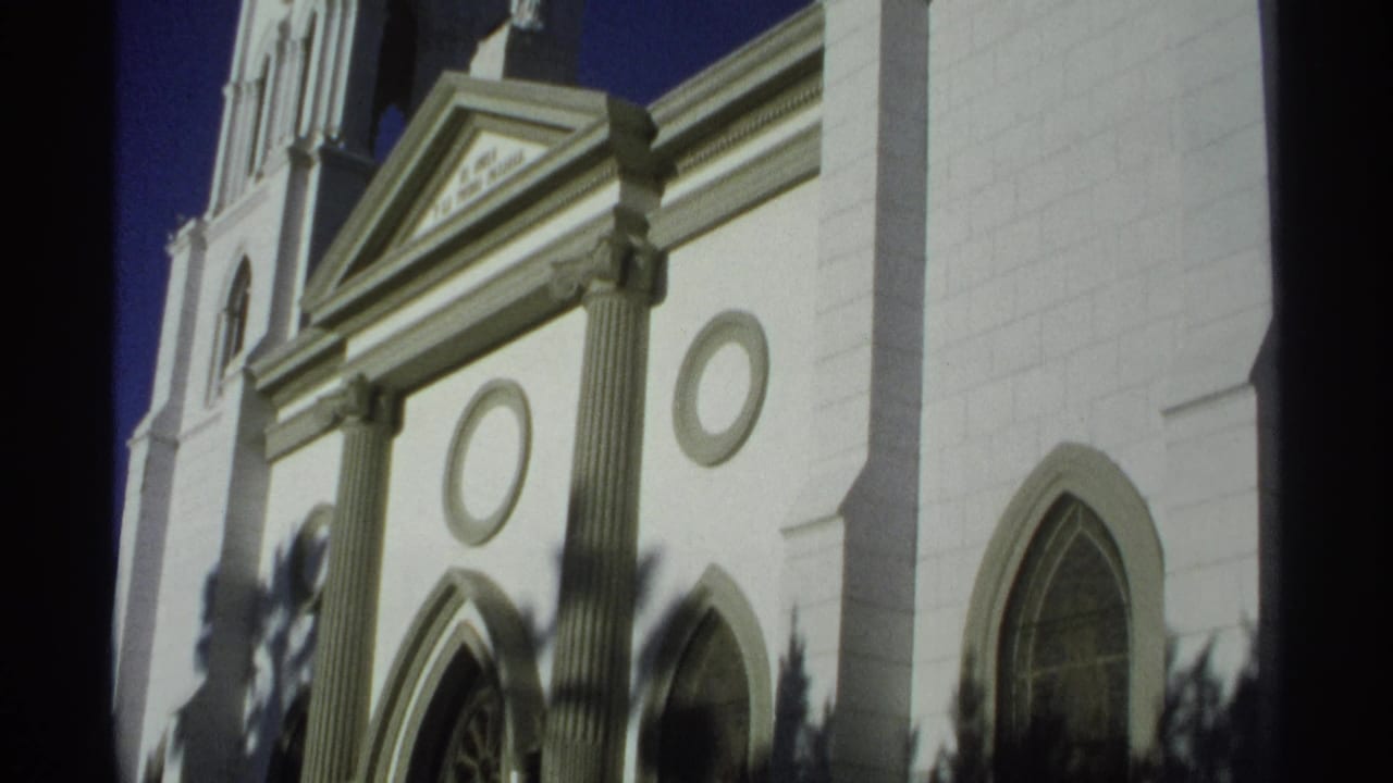 1970s 8mm view of San Fernando Cathedral's triangular pediment, columns and white wall under strong sunlight.