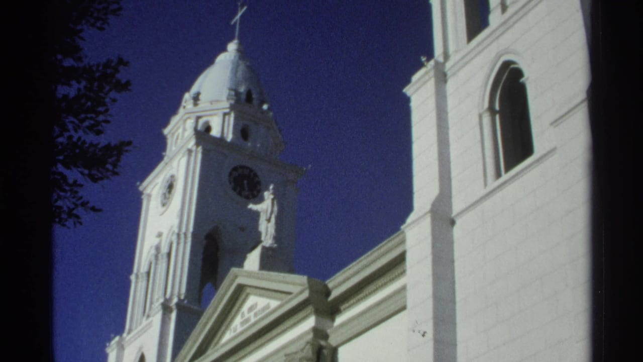 Second low-angle view of the white church tower, clock, dome, statue, and adjoining facade.