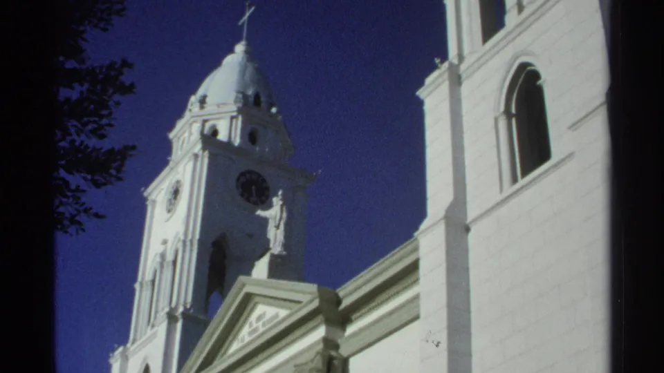 1975 Guaymas frame with the church tower, clock face, domed top, statue, and pale facade in strong sunlight.
