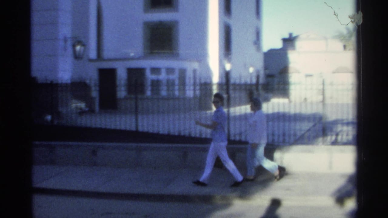 Two women walk past a white building and black iron fence.