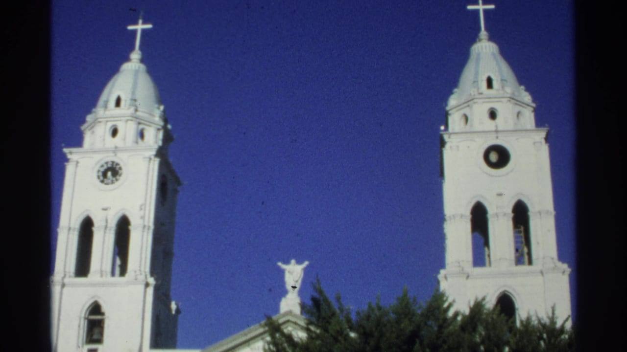 1975 Guaymas, Mexico frame with a low-angle view of white cathedral towers, domed crosses, arched openings, a statue, and trees.