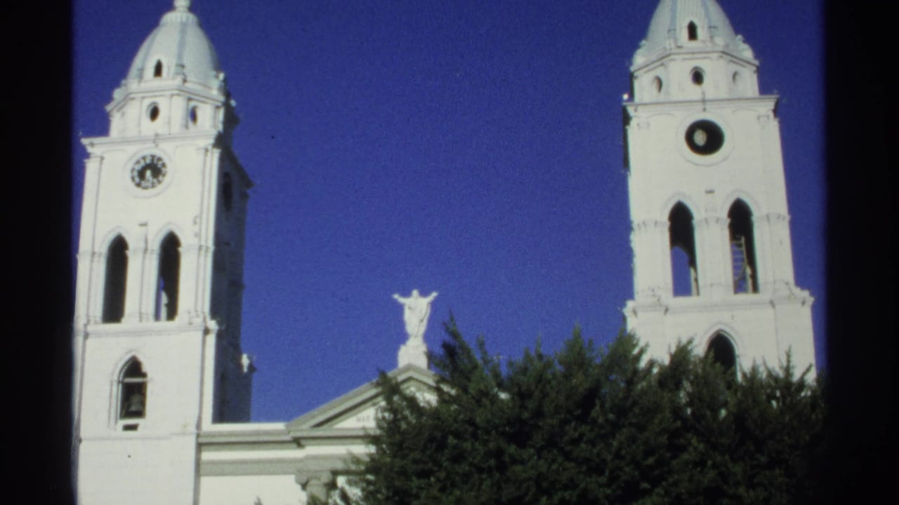 1975 Guaymas, Mexico frame of white cathedral towers against blue sky, with domed crosses, arched openings, a central statue, and trees.