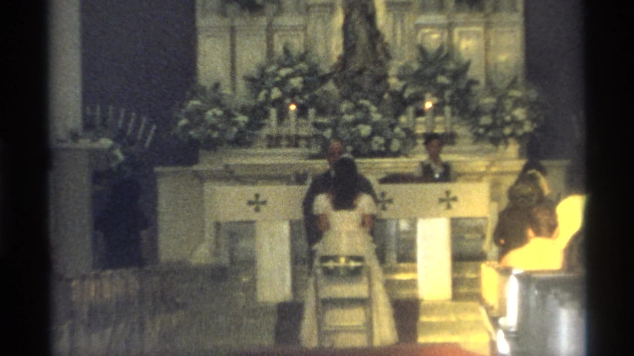 Wedding couple and priest remain at the altar with flowers and candles behind them.